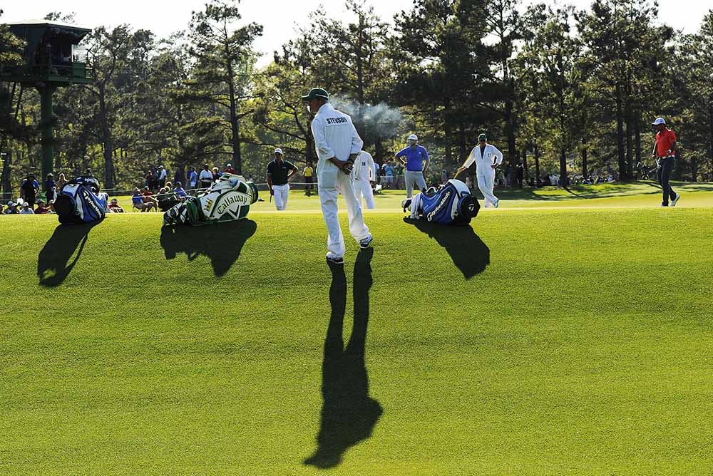 Henrik Stenson's caddie Gareth Bryn Lord (centre) smokes as golfers play during the first round of the 78th Masters Golf Tournament at Augusta